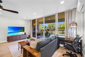 A modern living room with a TV, sofa, coffee table, and a balcony with a view. -  Kihei Kai Nani Beachside Resort Vistas (Kihei)