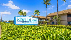 A sign for Kihei Kai Nani Vacation Resort with a clear view of the building and surrounding greenery. -  Kihei Kai Nani Beachside Resort Vistas (Kihei)