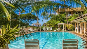 A clear blue pool surrounded by palm trees and lounge chairs, with a gazebo and a building in the background. -  Kihei Kai Nani Beachside Resort Vistas (Kihei)