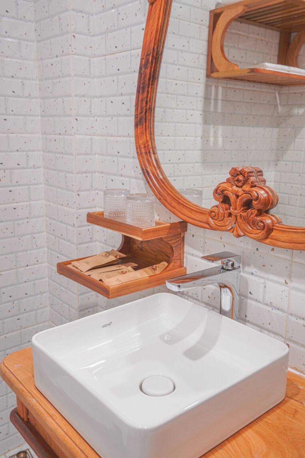 A bathroom with a white sink, wooden vanity, and a mirror with an ornate wooden frame.