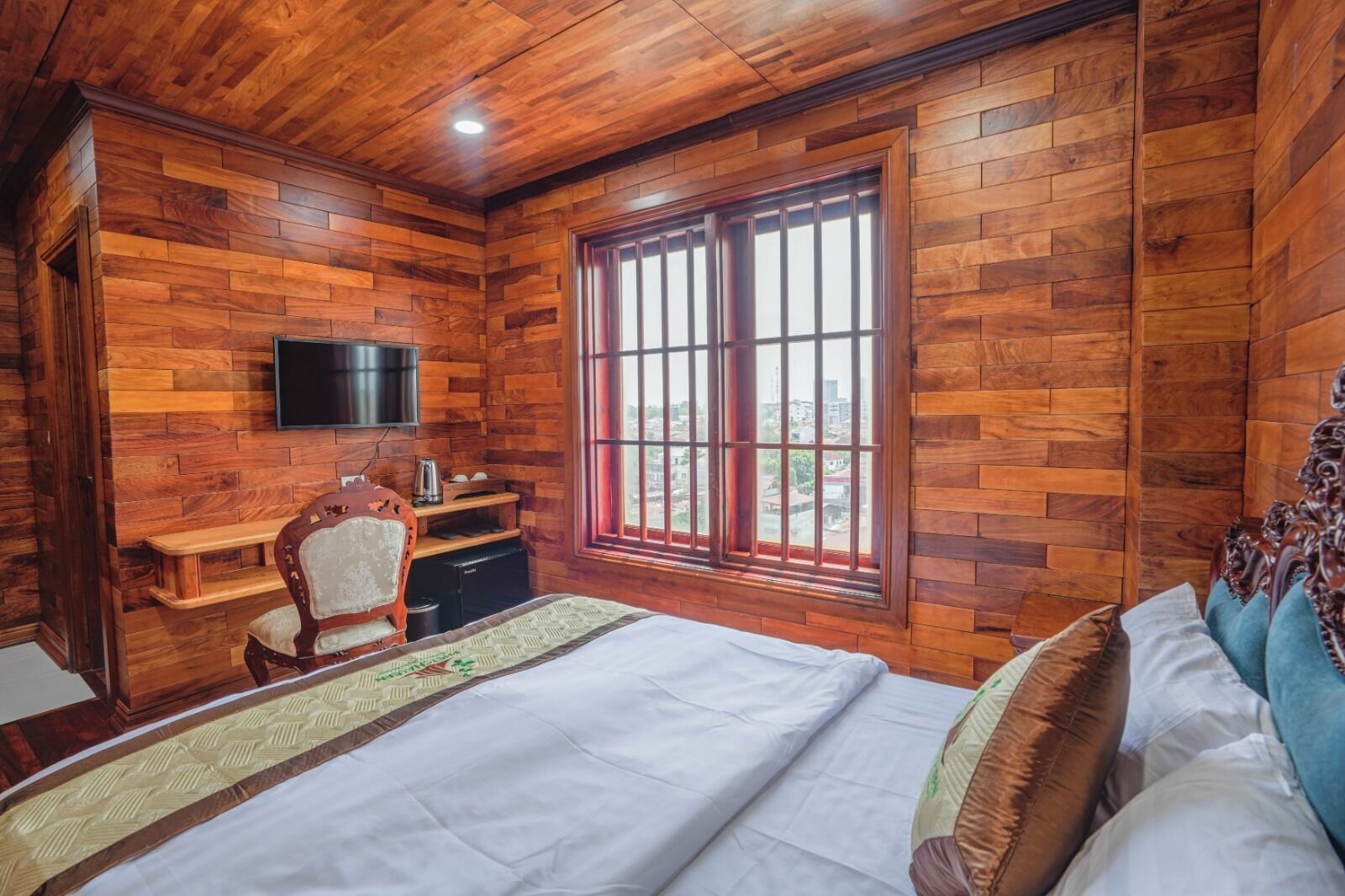 A wooden-paneled room with a bed, a desk, a chair, and a TV.
