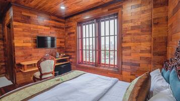 A wooden-paneled room with a bed, a desk, a chair, and a TV.