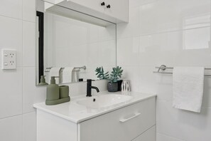 Un bany modern amb un lavabo blanc, aixeta negra i un mirall a sobre. Hi ha dues plantes en testos al taulell i una tovallola blanca penjant d'un suport.