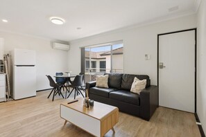 Un saló modern amb un sofà de pell negra, una taula de centre de fusta i una zona de menjador amb taula blanca i cadires negres.