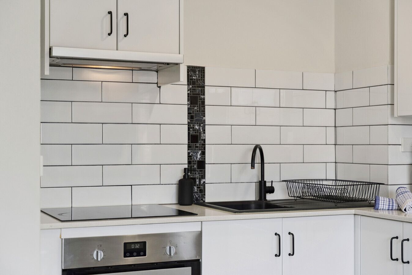 A kitchen with white cabinets, a black faucet, and a stainless steel oven.