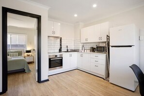 A modern kitchen with white cabinetry, a built-in oven, a microwave, and a refrigerator. - Charming Riverside Foreshore (South Perth)