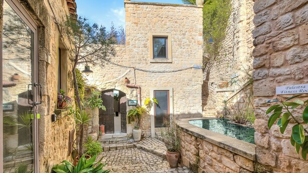 A stone courtyard with a pool, potted plants, and a sign for 'Palestra Fitness Room.'