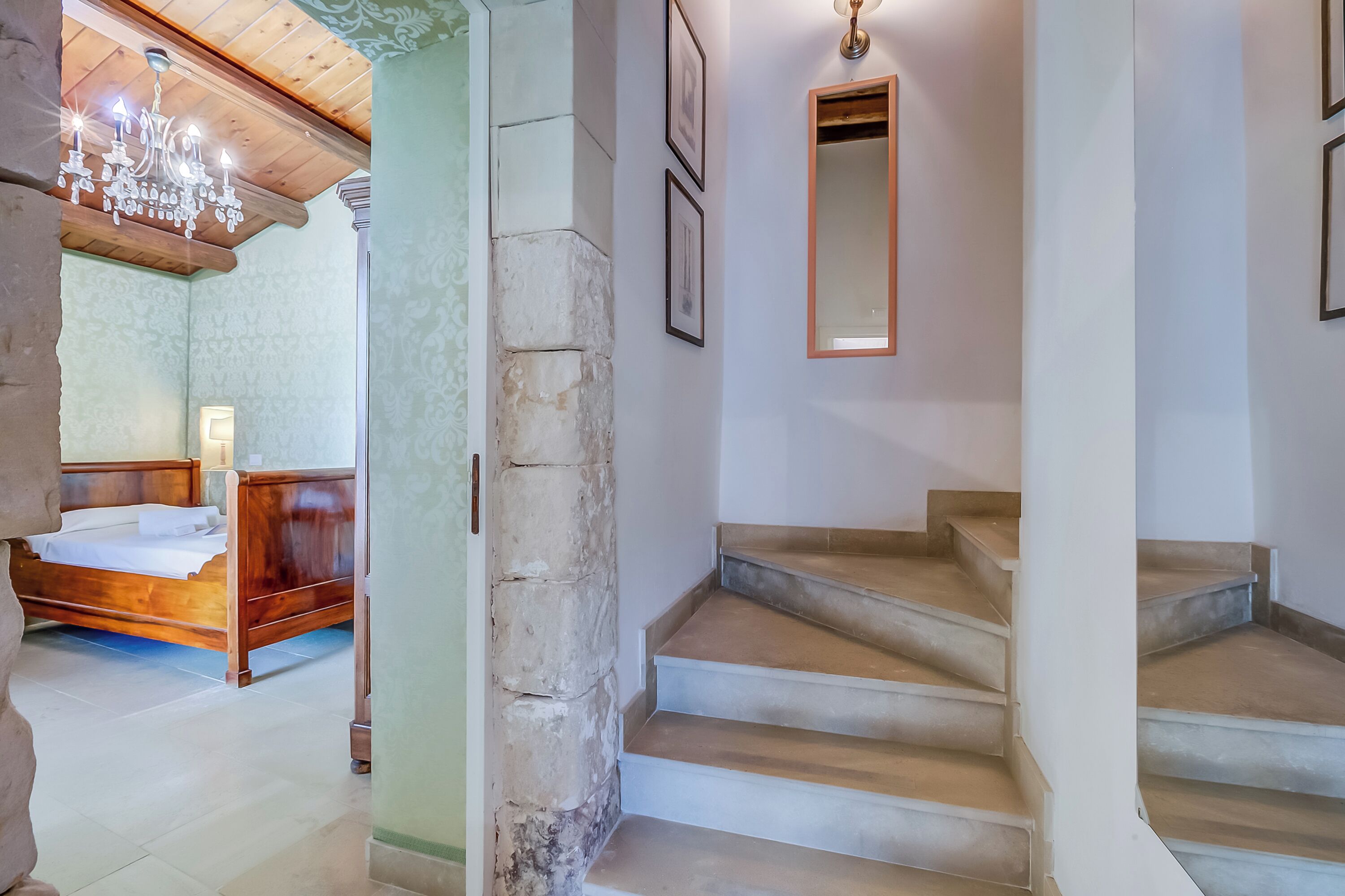 A staircase leading to a bedroom with a wooden bed and a chandelier.