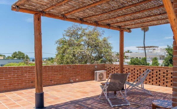 Ein überdachter Außenbereich mit Backsteinmauer, einer Holzpergola und einer Sitzecke mit zwei Stühlen.