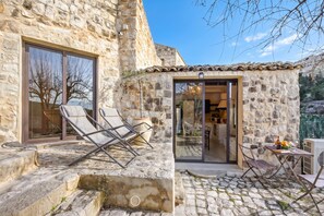 A stone building with a glass door entrance, a small patio with a table and chairs, and a lounge chair outside. - Borgo Hedone - Jardin, Scicli, Italy (Scicli)