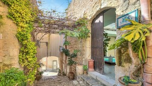 Un escalier en pierre mène à un bâtiment sur lequel on peut voir une enseigne, des plantes en pot et d’où l’on aperçoit une piscine.