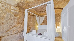 Une chambre aux murs de pierre, dotée d’un lit à baldaquin, de linge de lit blanc et d’une table de chevet avec une lampe.
