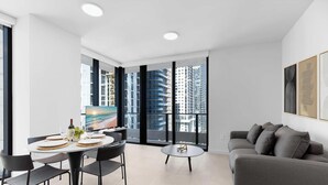 Una sala de estar moderna con comedor, ventanas amplias, un sofá gris y obras de arte en la pared.