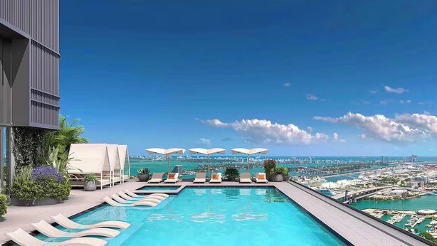 Piscina infinita en la azotea con sillones de descanso y sombrillas, con vistas a un paisaje urbano y la costa.