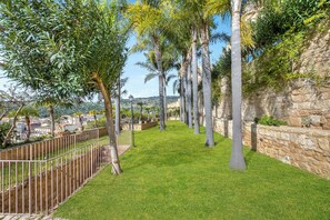 A landscaped garden with a stone wall, a metal fence, and a variety of trees.