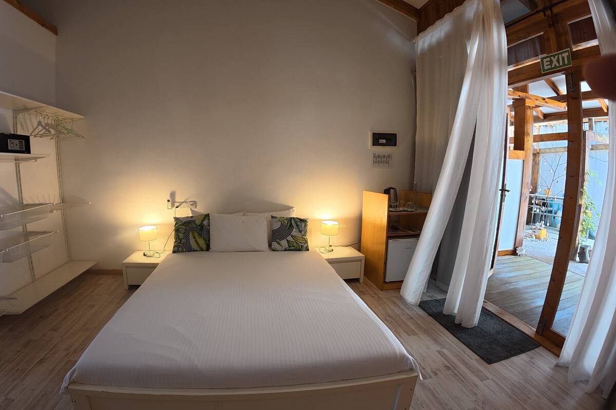 Une chambre à coucher avec un lit, des tables de chevet, un bureau et une vue sur l’extérieur.