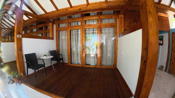 A wooden-framed room with a glass door, a small table with chairs, and a potted plant.