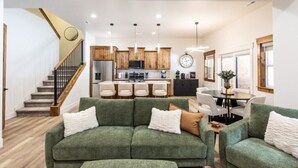 Una sala de estar moderna con un sofá verde, una escalera y una zona de cocina con armarios de madera y un reloj.