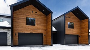 Un edificio moderno con dos puertas de garaje, revestimiento de madera y un cielo despejado.