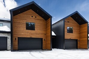 Ein modernes Gebäude mit zwei Garagentoren, Holzfassade und blauem Himmel.