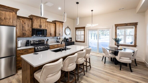 Una cocina moderna con armarios de madera, electrodomésticos de acero inoxidable, una isla grande con taburetes de bar, luces colgantes y un comedor con mesa y sillas.