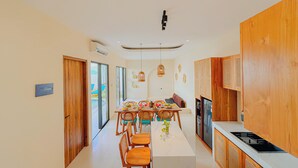 A modern kitchen with wooden cabinets, a dining area with a long table and chairs, and a TV. - Beachside Luxury 3BR Mediterranean Sanur (Denpasar)