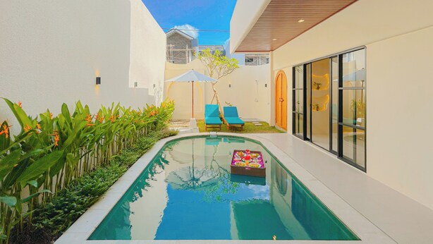 A modern pool area with a clear blue pool, lounge chairs, and a small table with flowers. - Beachside Luxury 3BR Mediterranean Sanur (Denpasar)