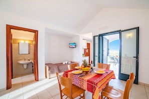 A dining area with a table set for two, a television mounted on the wall, and a view of the outdoors through a sliding door. - Beach in 5 min | Pool Access | n.64, Otranto, Italy (Otranto)