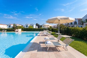 A swimming pool with lounge chairs and umbrellas, surrounded by greenery and buildings. - Beach in 5 min | Pool Access | n.64, Otranto, Italy (Otranto)