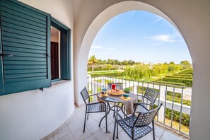 A balcony with a table set for two, overlooking a well-manicured garden and distant buildings. - Beach in 5 min | Pool Access | n.64, Otranto, Italy (Otranto)