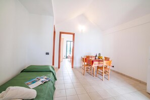 Ein Zimmer mit einem Bett, einem Esstisch mit Stühlen und Blick durch eine offene Tür.