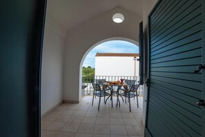 Eine offene Tür führt zu einem Balkon mit Tisch und Stühlen und Blick auf ein Gebäude. Der Boden ist mit Fliesen ausgelegt.