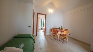 Un dormitorio con una cama verde, una zona de comedor con una mesa y sillas, y un pasillo que conduce a otra habitación.