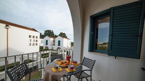 Un balcón al aire libre con una mesa lista para el desayuno, sillas y vistas a edificios.