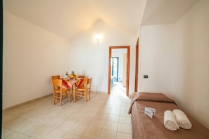 A room with a bed, a dining table with chairs, and a corridor leading to another room.