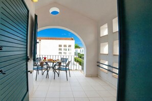 An open balcony with a table and chairs, a view of a building, and a door leading to the balcony.