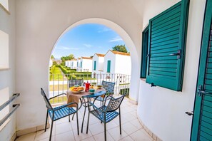 A balcony with a table, chairs, and a view of white buildings with green shutters. - Beach in 5 min | Pool Access | n.58, Otranto, Italy (Otranto)