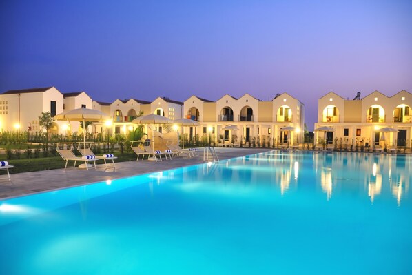 A hotel with a swimming pool, sun loungers, and umbrellas.