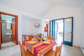 A dining area with a table set for two, a kitchen in the background, and a sliding glass door leading to an outdoor area. - Beach in 5 min | Pool Access | n.56, Otranto, Italy (Otranto)