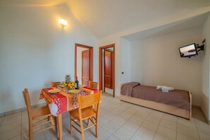 A room with a dining table set for two, a bed with a TV, and a wall-mounted light. - Beach in 5 min | Pool Access | n.56, Otranto, Italy (Otranto)