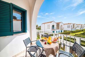 A balcony with a table set for breakfast, overlooking a row of white buildings with green shutters.