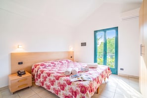 A bedroom with a bed, bedside table, and a view of greenery through a door. - Beach in 5 min | Pool Access | n.56, Otranto, Italy (Otranto)