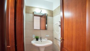 A bathroom with a wooden door, a white sink, a mirror, and a handheld showerhead. - Beach in 5 min | Pool Access | n.56, Otranto, Italy (Otranto)