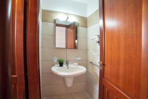 Un bagno con una porta in legno, un lavandino bianco, uno specchio e un soffione doccia a mano.