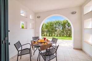 Ein Essbereich mit einem Tisch, gedeckt für vier Personen, umgeben von Stühlen, und einem Durchgang zu einem Garten.