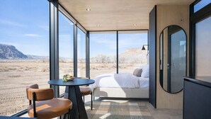 A modern room with a bed, a dining table, and chairs. It has large windows offering a view of a desert landscape. - Reflections (Torrey)
