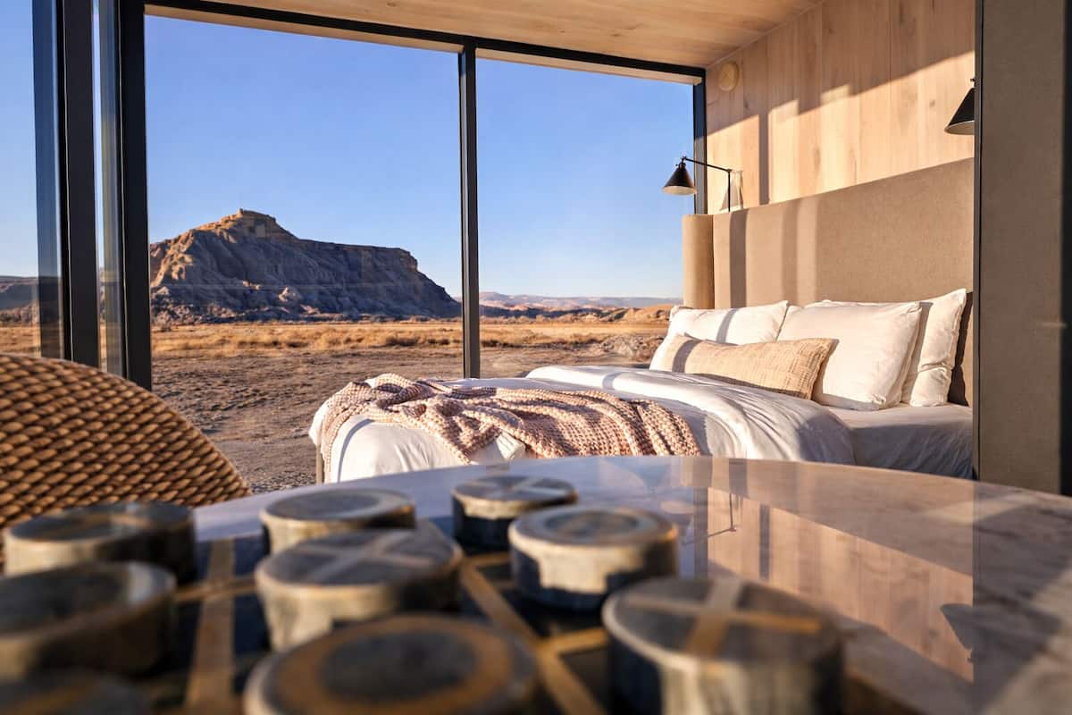 A modern bedroom with a large window, a bed, and a wooden table with logs.