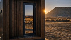 A wooden cabin with a door, a view of a desert landscape, and a mountain range in the background. - Reflections (Torrey)