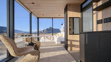 Un interior moderno con ventanas amplias, una cama, sillas de mimbre y vistas a un paisaje desértico.