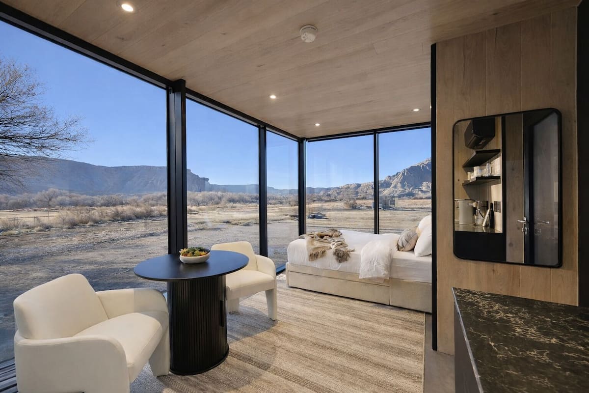 A modern interior with a large window, a sofa, a round table, and a kitchen area.